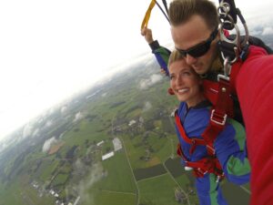 Excited couple enjoying tandem skydiving with stunning aerial view below.